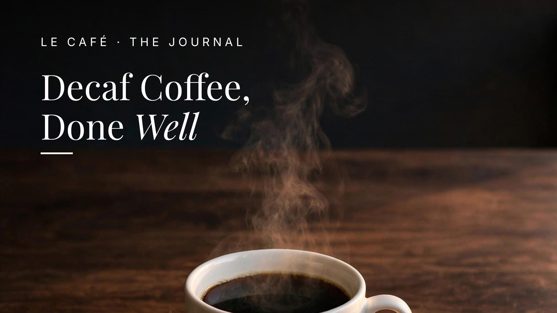 A white cup of steaming black coffee on a dark wood table in soft evening light. Le Café Journal header: Decaf Coffee, Done Well