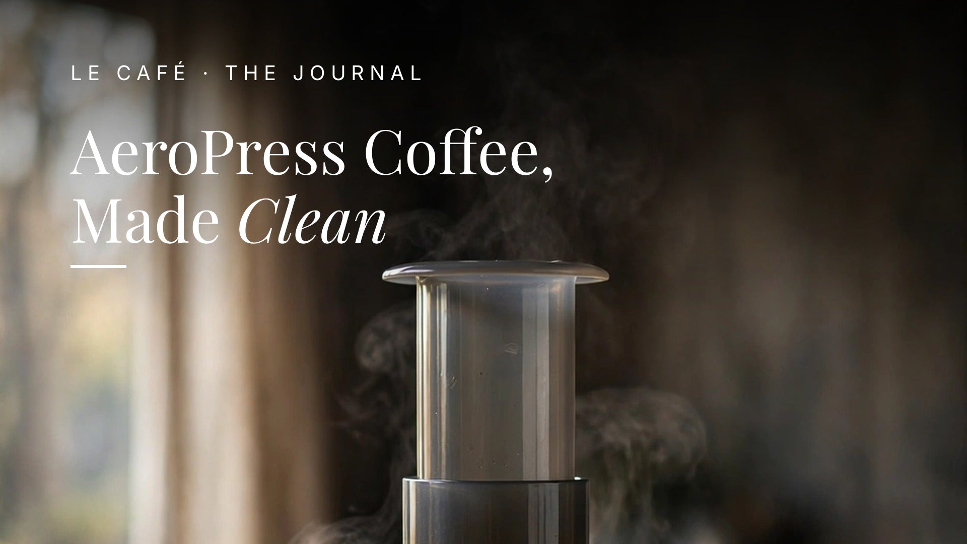 An AeroPress brewer pressing coffee into a clear glass cup on a dark wood table in soft morning light, with whole beans nearby. Le Cafe Journal header: AeroPress Coffee, Made Clean