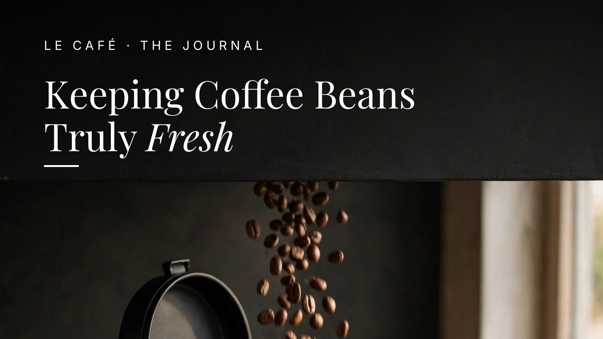 Coffee beans pouring into a matte black airtight canister on a dark wood counter beside a small ceramic cup in soft morning light. Le Cafe Journal header: Keeping Coffee Beans Truly Fresh
