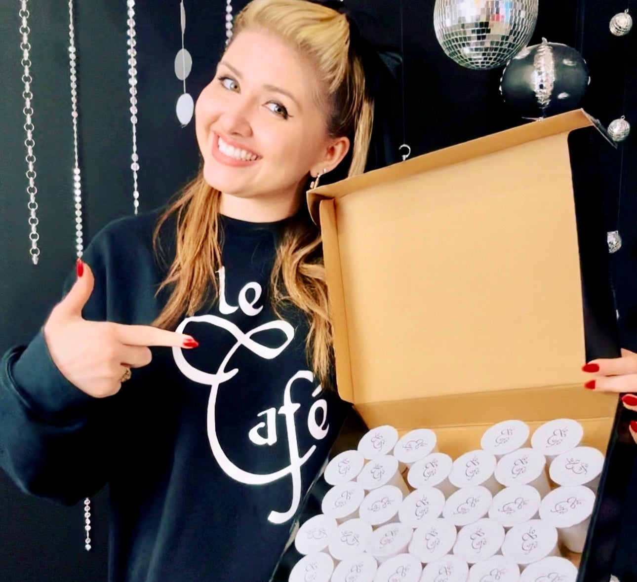 Nechama Henderson holding a box of white K-cups against a black background with decorative elements.