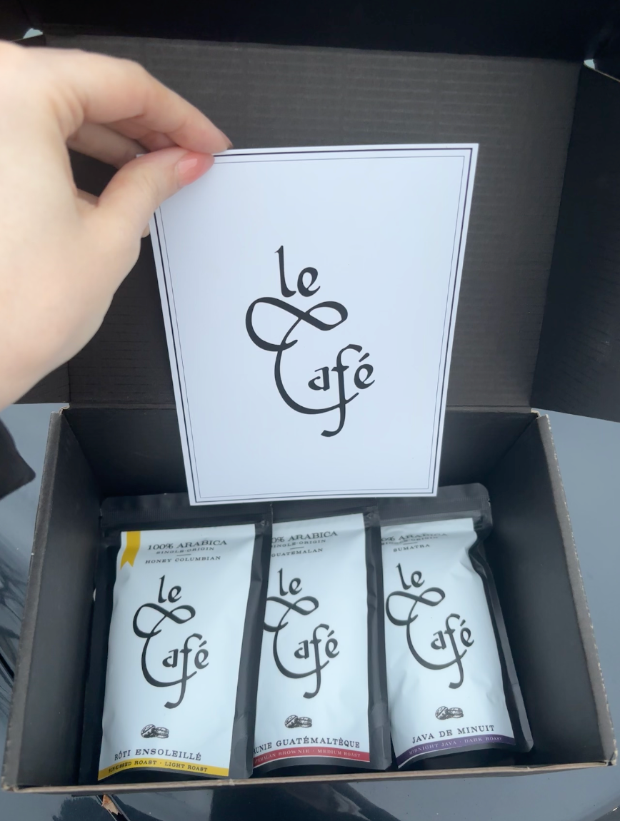 Box of 'Le Cafe' coffee packages with a card held above it.